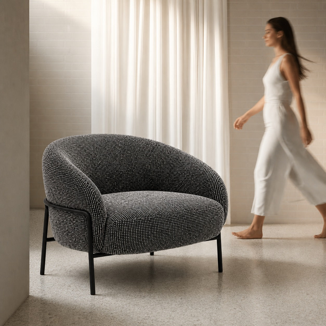 Gray textured armchair in a room with a woman in white clothing walking by.