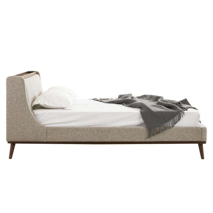 Beige upholstered bed with white bedding and a gray blanket on a white background
