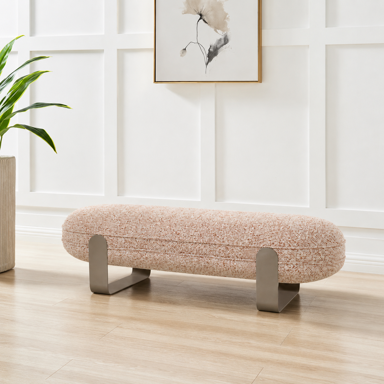 Beige ottoman with metal legs in a room with a plant and wall art.