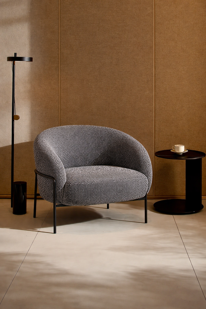 Gray armchair in a room with a brown wall and black side table.