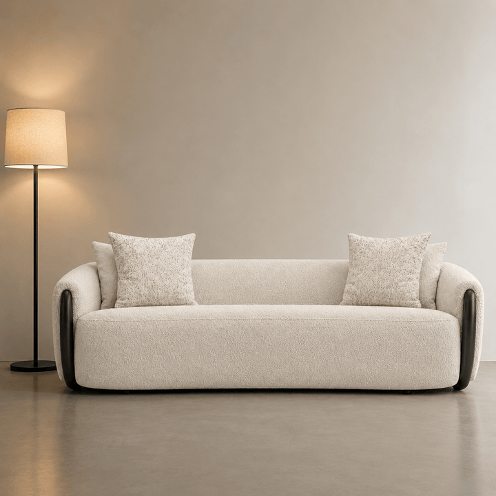 Beige sofa with two cushions in a room with a lamp and neutral walls.