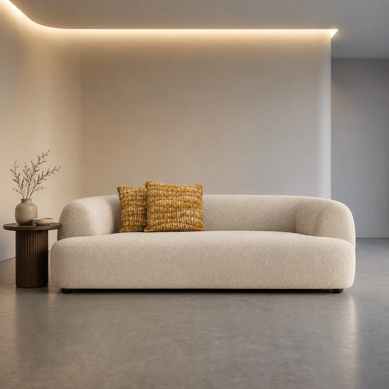 Beige sofa with two patterned cushions in a modern room with neutral walls and a small table.