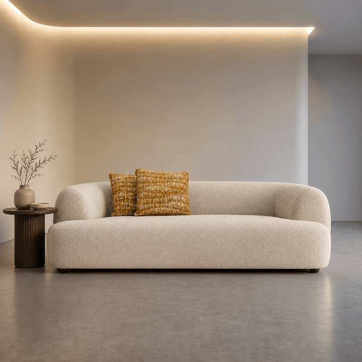Beige sofa with two patterned cushions in a modern room with neutral walls and a small table.