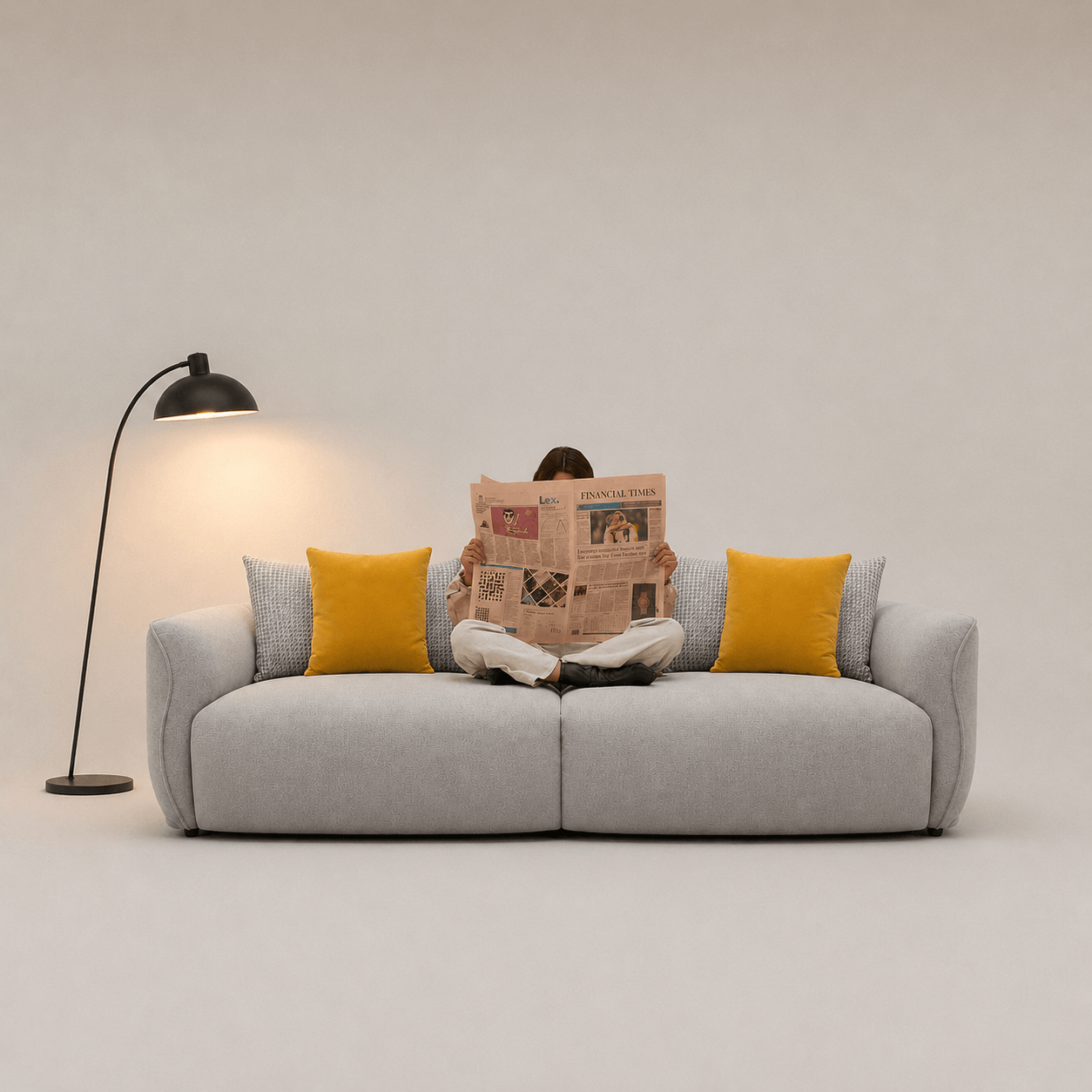 Person reading a newspaper on a gray sofa with yellow cushions, in a minimalistic room.