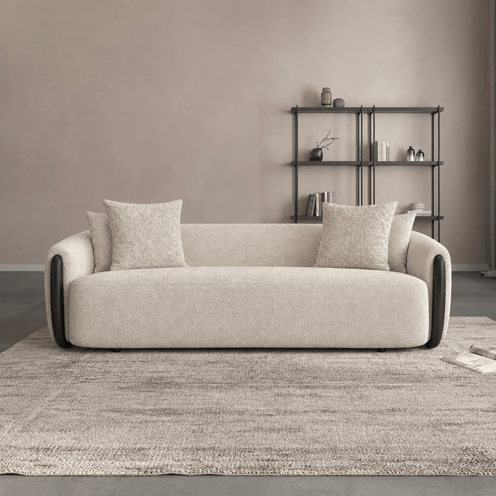 Beige sofa with cushions in a room with a bookshelf and rug.