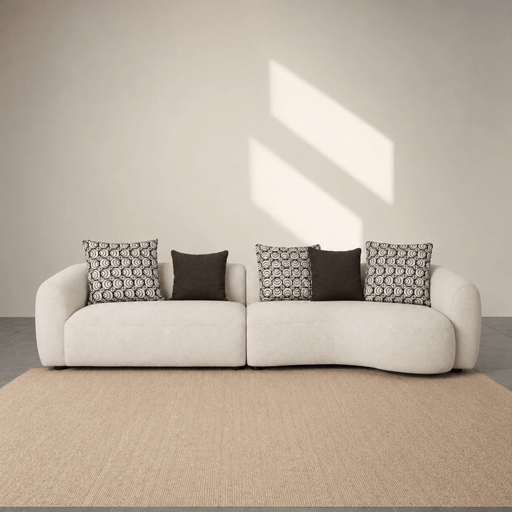 White sofa with patterned cushions in a minimalistic room with sunlight streaming through a window.