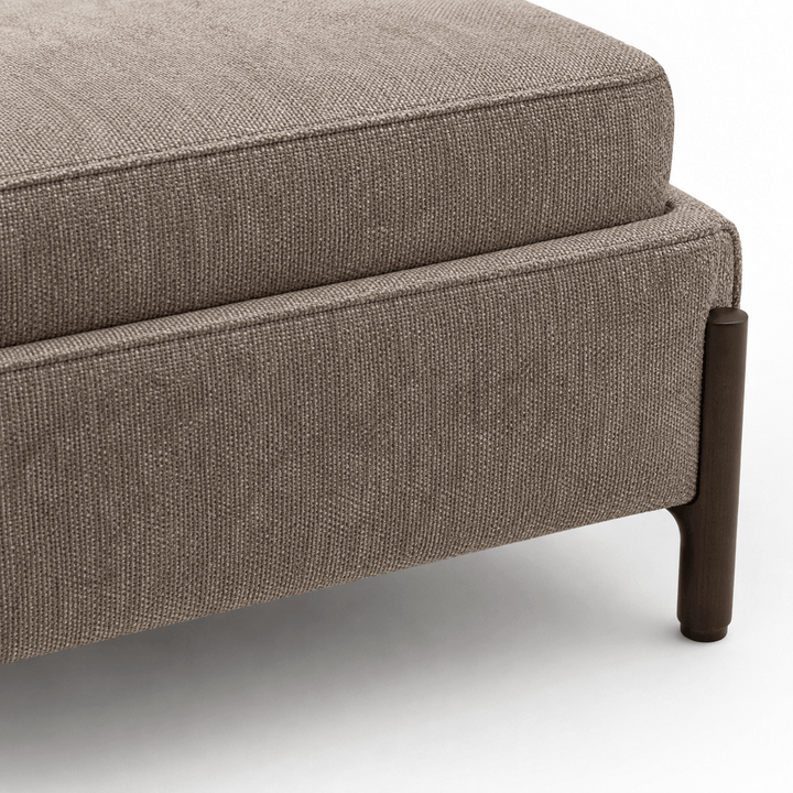 Brown upholstered ottoman with a wooden leg on a white background