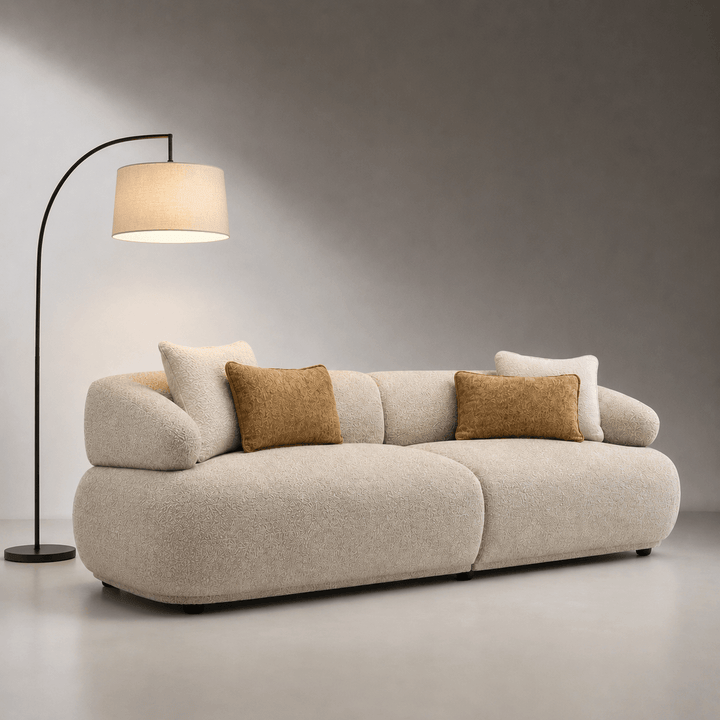 Beige sofa with decorative pillows in a minimalistic room with a floor lamp.