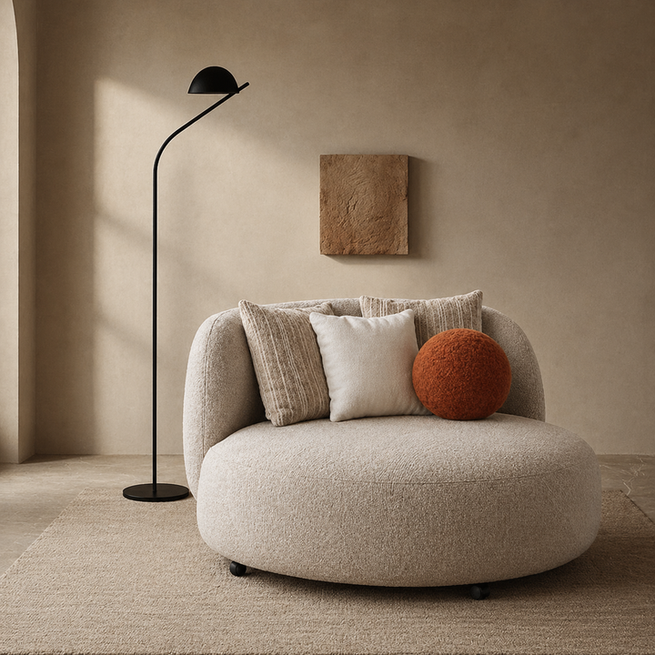 Modern beige armchair with cushions in a minimalistic room with a floor lamp and wall art.