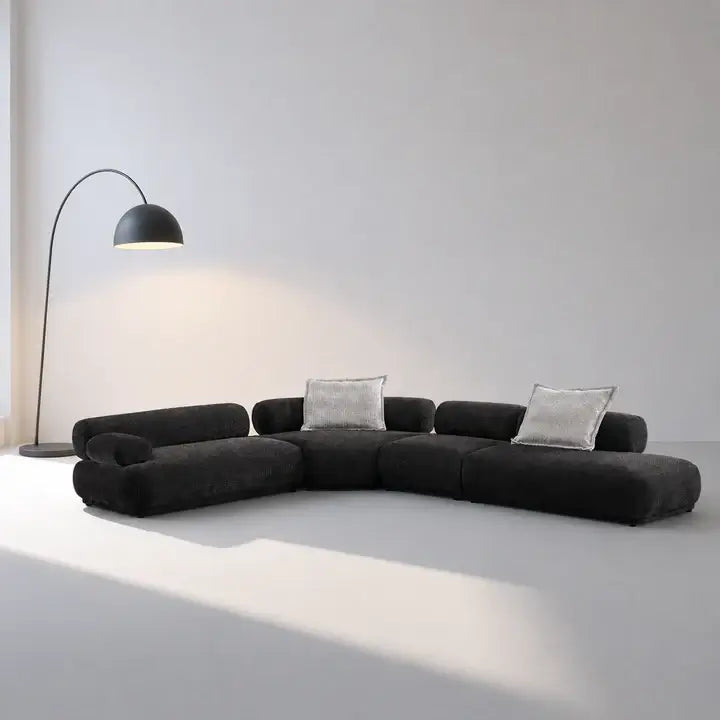 Modern black sectional sofa with gray cushions in a minimalistic room.