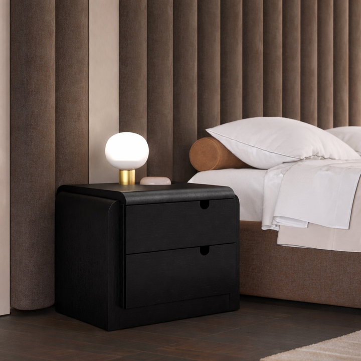 Black nightstand with a lamp next to a bed in a bedroom setting