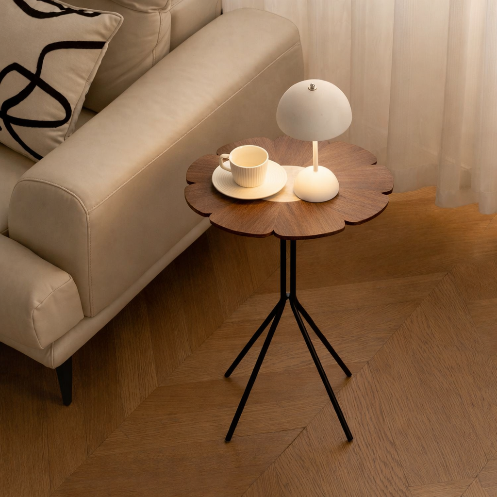 Small round table with a lamp and cup next to a beige sofa in a living room.
