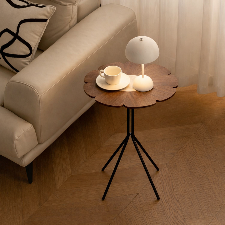 Small round table with a lamp and cup next to a beige sofa in a living room.